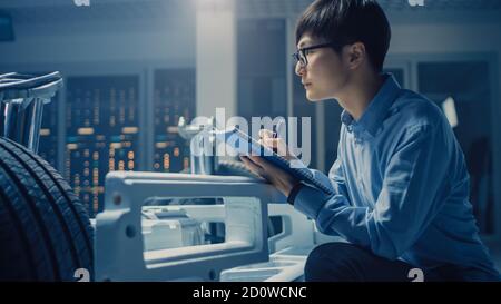 Le concepteur automobile assis à côté de la plate-forme hybride de châssis de voiture électrique, écrit des estimations et des esquisses dans le Bloc-notes. Installation avec châssis de véhicule Banque D'Images