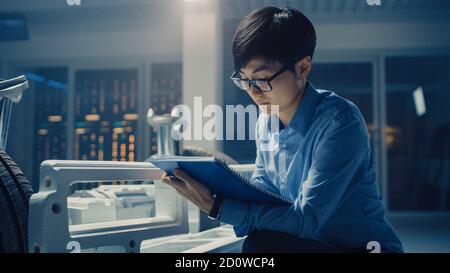 Le concepteur automobile assis à côté de la plate-forme hybride de châssis de voiture électrique, écrit des estimations et des esquisses dans le Bloc-notes. Installation avec châssis de véhicule Banque D'Images