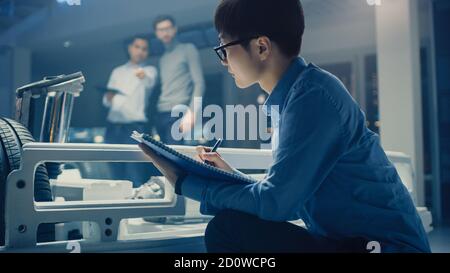 Le concepteur automobile assis à côté de la plate-forme hybride de châssis de voiture électrique, écrit des estimations et des esquisses dans le bloc-notes. Installation avec châssis de véhicule Banque D'Images