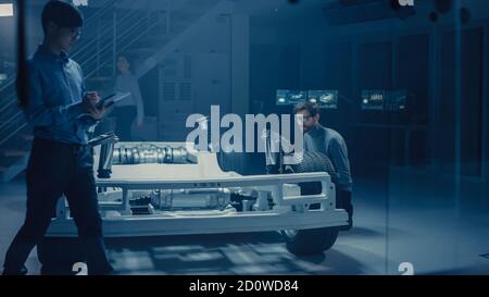 Ingénieur concepteur automobile assis à côté de la plate-forme de châssis de voiture électrique hybride, utilisant un Tablet Computer pour l'amélioration de la conception. Installation avec véhicule Banque D'Images