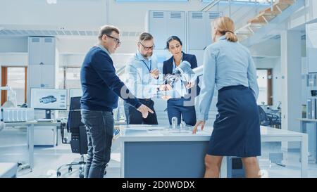 Diverses équipes d'ingénieurs en robotique industrielle se sont rassemblées autour de la table avec le bras de robot, ils utilisent un Tablet PC pour manipuler et programmer le pick up Banque D'Images