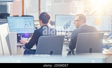 Vue arrière de l'équipe d'ingénieurs technologiques travaillant sur des ordinateurs de bureau dans Bright Sunny Office avec Sun Flare. Les écrans affichent le logiciel IDE/CAD Banque D'Images