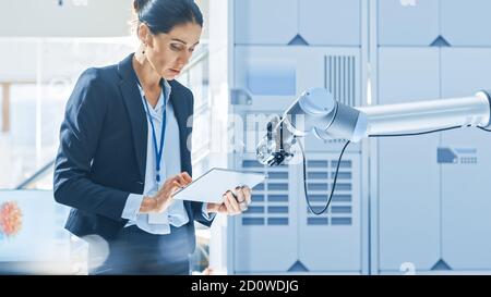 L'ingénieure en robotique industrielle féminine utilise une tablette pour programmer et manipuler le bras du robot pour le levage et le déplacement d'objets. Recherche technologique Banque D'Images