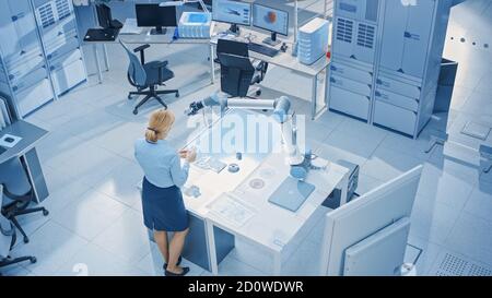 L'ingénieure féminine en robotique industrielle s'intéresse aux méthodes d'ingénierie Blueprints pour programmer et manipuler le bras du robot pour le levage et le déplacement d'objets Banque D'Images