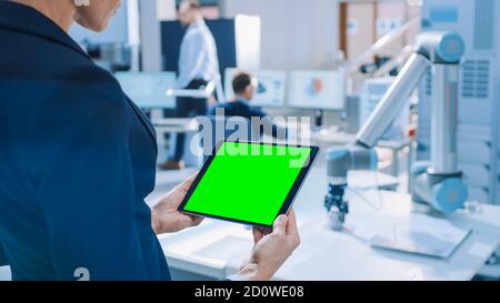 L'ingénieur possède une tablette numérique à écran maquette vert. Dans l'équipe d'arrière-plan des ingénieurs industriels travaillant avec le bras du robot fonctionnel dans Banque D'Images