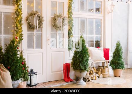 La maison privée blanche est décorée de petits arbres de Noël et de lanternes, un sac de cadeaux. Un banc avec des oreillers près de la porte avant de la maison an Banque D'Images