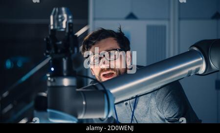 Photo d'un ingénieur mécanique travaillant avec un bras robotique futuriste. Le robot déplace un objet métallique. Laboratoire de recherche haute technologie avec équipement moderne. Banque D'Images