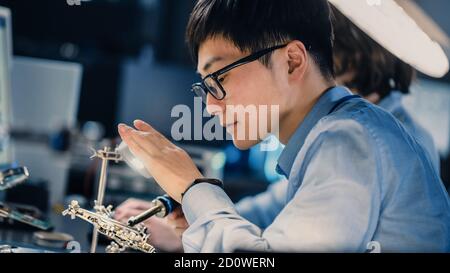 Gros plan sur un ingénieur de développement électronique japonais professionnel dans Chemise bleue souillée d'une carte de circuit imprimé dans une haute technologie Laboratoire de recherche avec Banque D'Images