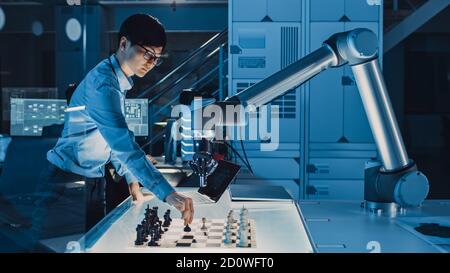 Un ingénieur de développement japonais professionnel teste une interface d'intelligence artificielle en jouant aux échecs avec un bras robotique futuriste. Ils sont dans Banque D'Images