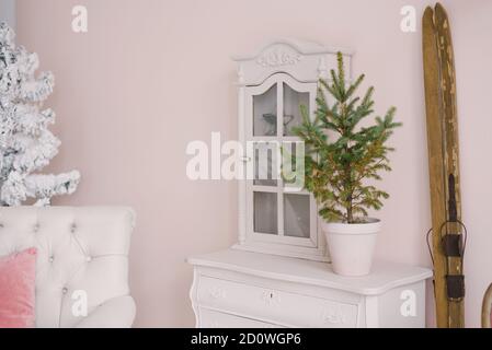 Un sapin de Noël dans une casserole en céramique se dresse sur un commode blanc dans le salon, décoré pour Noël ou le nouvel an. Support de skis en bois rétro près du Banque D'Images