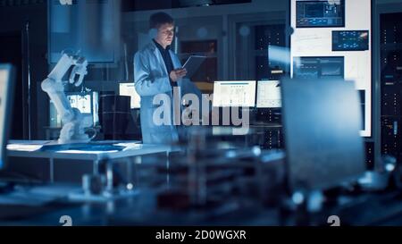 L'ingénieur robotique professionnel de l'industrie lourde porte un manteau blanc tenant l'ordinateur tablette passe dans le laboratoire. Installation pleine d'ordinateurs, divers Banque D'Images