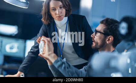 Un ingénieur futuriste de développement de machines-moteurs travaillant sur l'ordinateur à son bureau, s'entretient avec une femme responsable de projet. Équipe de professionnels travaillant dans Banque D'Images