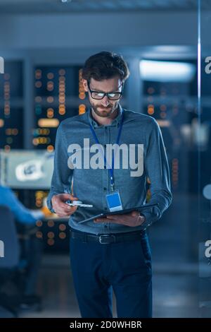 Dans l'installation de recherche technologique : l'ingénieur en chef est au milieu du laboratoire et utilise un Tablet PC. Équipe d'ingénieurs industriels, développeurs Banque D'Images
