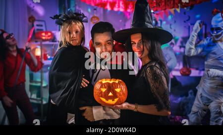 Halloween Costume Party: Père Count Dracula tient petite fille de Bat et la femme de Hugs Witch pour un portrait de famille heureux. En arrière-plan Banque D'Images