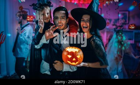 Halloween Costume Party: Père Count Dracula tient petite fille de Bat et la femme de Hugs Witch pour un portrait de famille heureux. En arrière-plan Banque D'Images