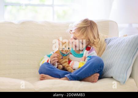 Enfant jouant avec chat. Enfant tenant chaton. Un petit garçon qui arrache un joli animal de compagnie assis sur le canapé dans le salon ensoleillé à la maison. Les enfants jouent avec les animaux de compagnie. C Banque D'Images