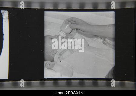 Fin années 1970 photographie en noir et blanc vintage d'un bébé allaitant à partir d'une bouteille de lait. Banque D'Images