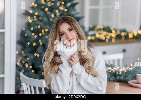 Belle blonde curly avec de longs cheveux près des arbres de Noël avec guirlande de lumières. Portrait en gros plan d'une jeune femme avec un sourire blanc dans un gris Banque D'Images