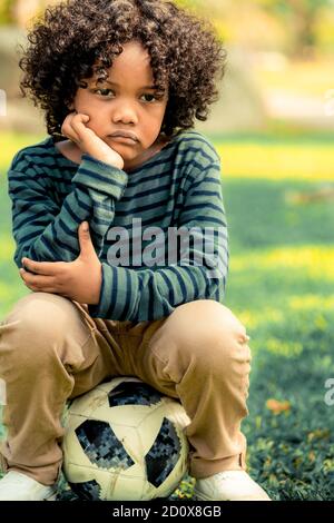 Peu ennuyé malheureux african american kid assis dans le parc. Le garçon montrant l'émotion négative. Le concept de l'enfant. Banque D'Images