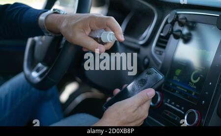 spray désinfectant pour les mains de sexe masculin sur l'écran de votre smartphone la voiture Banque D'Images
