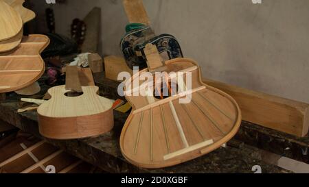 Deux guitares en bois dans le processus d'assemblage avec presses maintenant les pièces sur l'établi du menuisier avec du gris mur en arrière-plan Banque D'Images