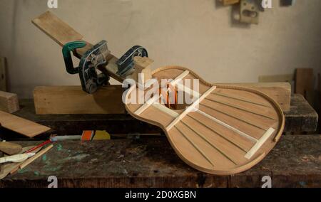 Guitare en bois dans le processus d'assemblage avec des presses tenant des pièces sur atelier de menuisier avec paroi grise en arrière-plan Banque D'Images