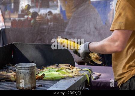 Un vendeur de rue prépare le maïs sur l'épi en le badigeonnant avec du beurre d'ail fondu et en le posant sur un barbecue. Banque D'Images