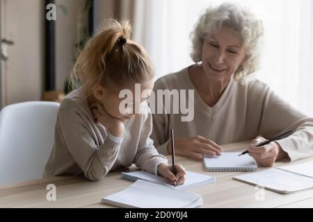 Grand-mère mûre souriante aidant petite-fille à faire ses devoirs à l'école Banque D'Images