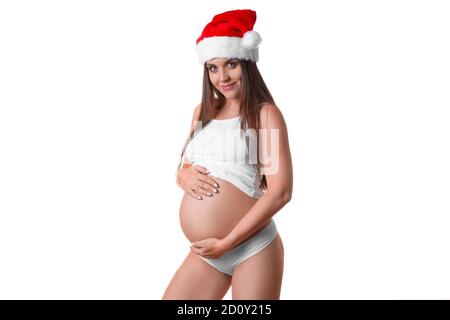 Femme enceinte smiley dans le chapeau de Santa tient doucement son ventre. Photo sur fond blanc. Banque D'Images