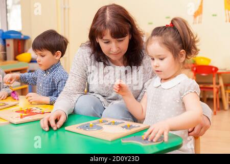 adulte belle femme de race blanche enseignant recueillir le puzzle avec une fille à la table verte dans la salle de classe. Image couleur horizontale Banque D'Images