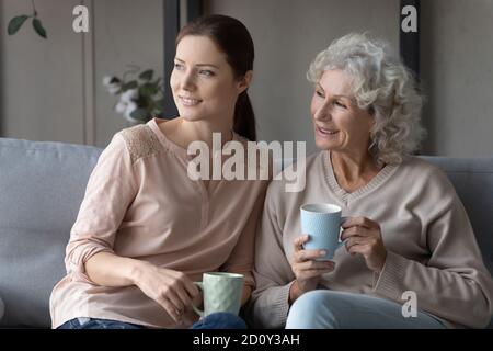Femme mûre souriante et rêveuse, avec une fille grognup qui boit du thé Banque D'Images