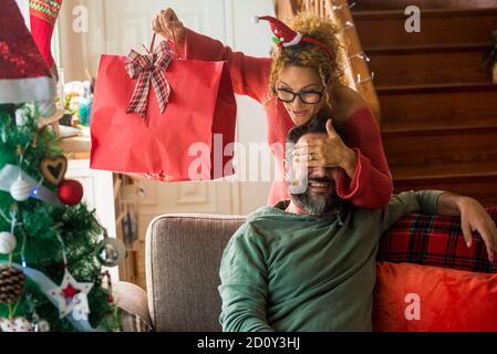 Concept de Noël et de saison des fêtes avec couple de gens heureux à la maison dans la surprise et cadeaux échange - bonheur et joyeuse avec la femme an Banque D'Images