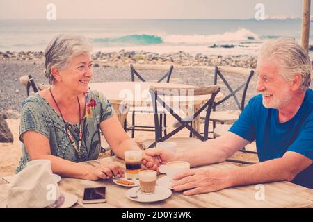 Vieux senior beau couple caucasien appréciez la relation et la vie ensemble boire un café au bar sur la plage - concept de mode de vie à la retraite an Banque D'Images