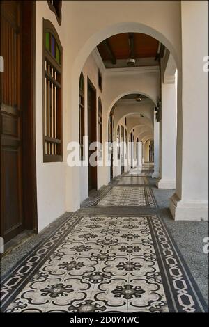 Une vue sur le sol le long d'un couloir de maisons traditionnelles chinoises peranakan, avec des colonnes voûtées et des sols carrelés ornés. Banque D'Images