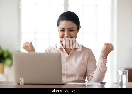 Une jeune femme ethnique surjoyeuse, excitée par les nouvelles sur ordinateur portable Banque D'Images