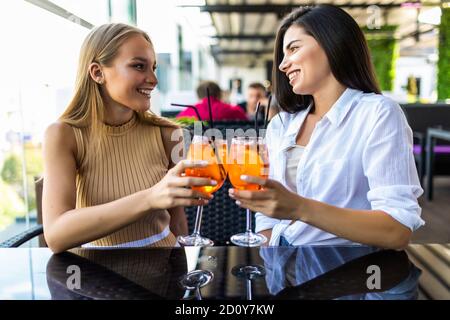 Jeunes femmes buvant aperol spritz, des verres de clin d'œil avec des amis, regardant l'appareil photo dans le café Banque D'Images