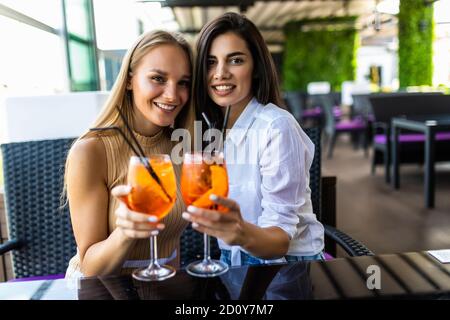 Jeunes femmes buvant aperol spritz, des verres de clin d'œil avec des amis, regardant l'appareil photo dans le café Banque D'Images