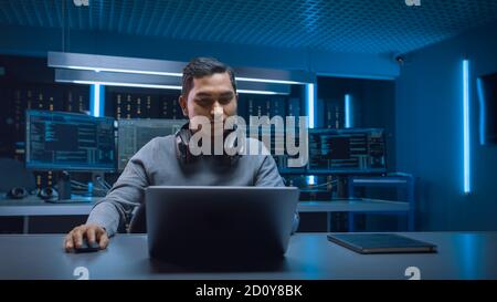 Portrait du beau développeur indien de logiciels Hacker Gamer portant un casque assis à son bureau et travaillant à jouer sur un ordinateur portable. En arrière-plan néon foncé Banque D'Images
