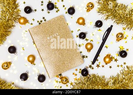Carnet doré avec couverture scintillante, boules de Noël dorées et noires, guirlande et étoiles confettis. Bilan de l'année, liste de souhaits, résolutions du nouvel an Banque D'Images