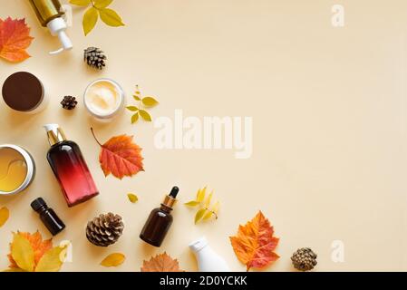 Produits de soin de la peau et feuilles d'automne sur fond jaune, couché à plat, espace de copie. Routine de beauté saisonnière d'automne et concept de soins organiques de la peau. Banque D'Images