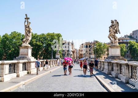 Les gens sur le pont Ponte Sant'Angelo marchant devant les statues baroques des anges avec des bâtiments de la ville et un ciel bleu en arrière-plan. Banque D'Images