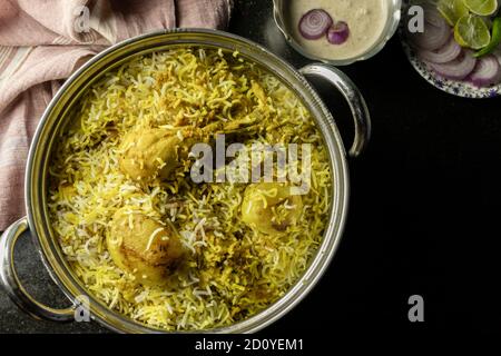 Poulet biryani délicieux et épicé fait maison dans un bol traditionnel avec raita et salade sur fond noir Banque D'Images