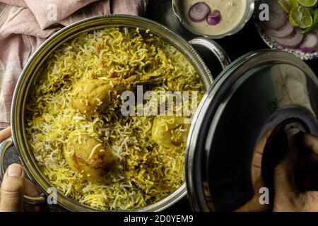 Poulet biryani délicieux et épicé fait maison dans un bol traditionnel avec raita et salade sur fond noir Banque D'Images