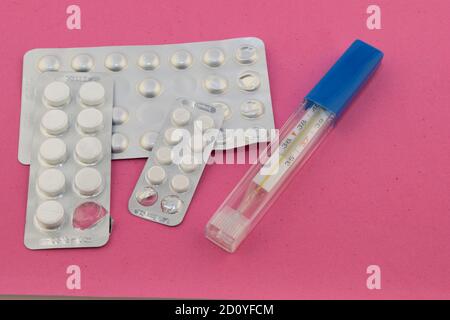 trois paquets de pilules et un thermomètre sont sur un rose arrière-plan en velours Banque D'Images