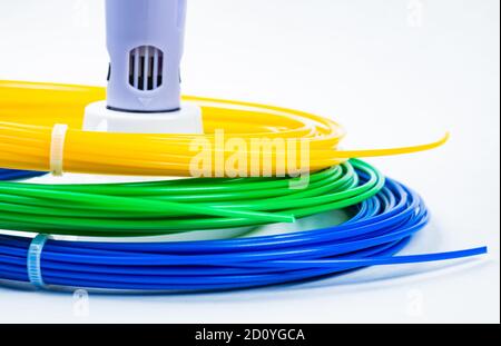 Gros plan sur un tas de câbles roulés colorés autour d'un stylo d'impression 3D pour enfants, isolé sur du blanc. Trois filaments en plastique lumineux couchés à l'intérieur. Conce Banque D'Images