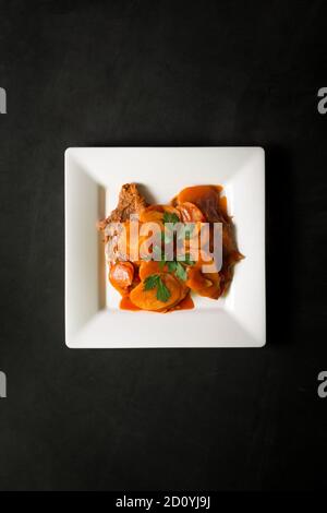 Steak avec carottes et pommes de terre sur une assiette blanche carrée sur fond noir Banque D'Images