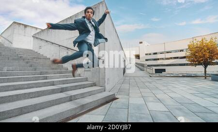 Joyeux et heureux homme d'affaires dans un costume tient le café et le saut en marchant sur les escaliers. Scène prise dans un parc en béton urbain à côté de Banque D'Images
