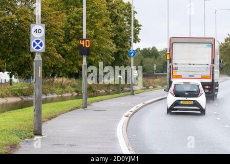 Circulation dépassant un panneau de limite de vitesse de 40 km/h, avec un indicateur de vitesse numérique qui affiche un avertissement de trafic. Route mouillée sous la pluie avec les véhicules qui passent. Banque D'Images