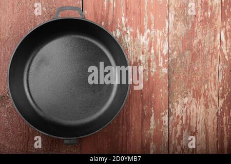 Poêle noire sans poignée sur fond en bois rouge. Espace pour le texte. Vue de dessus. Banque D'Images