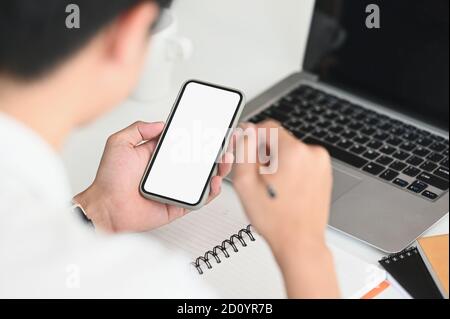 Homme d'affaires tenant le smartphone avec un écran vide. Travail sur ordinateur portable sur bureau . Banque D'Images